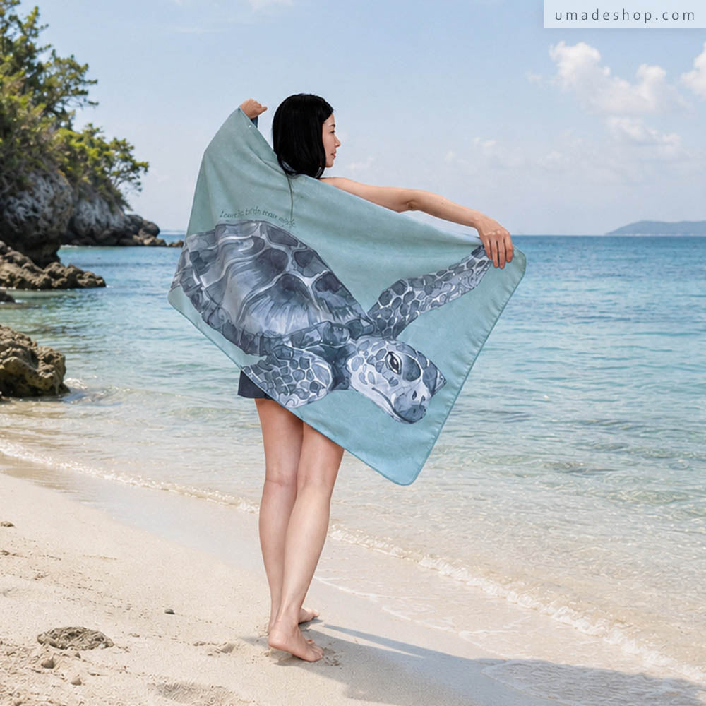 Umade 海洋微笑系列萬用快乾巾海龜款，對著海景披著海龜款快乾巾，展現夏日海邊渡假感。快乾毛巾具備3分鐘速乾、高吸水、輕巧好收納，不易有異味等功能，是夏日旅遊玩水必備品。