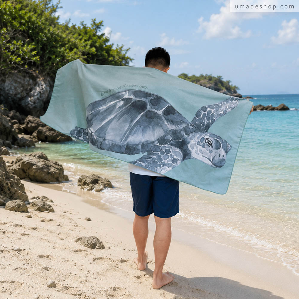 Umade 海洋微笑系列萬用快乾巾海龜款，站在沙灘上展示海龜圖案快乾巾，適合海邊玩水使用。SUP、游泳、衝浪、潛水、日光浴都適合，
